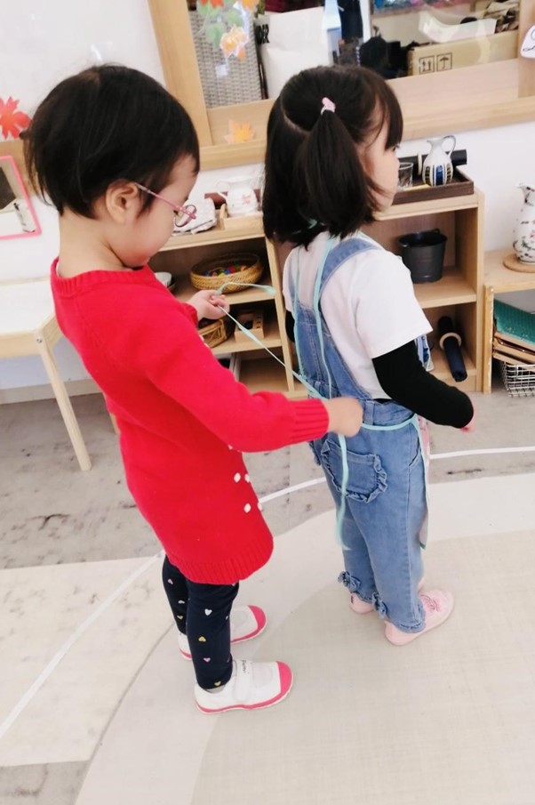 A four year old child helping another child tie their apron.
