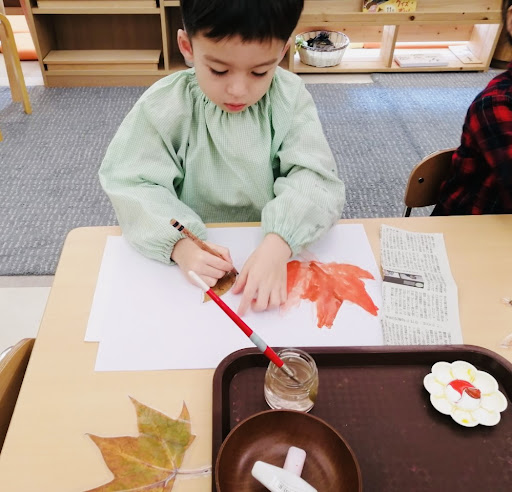 A child tracing a leaf and painting the shape with watercolor.